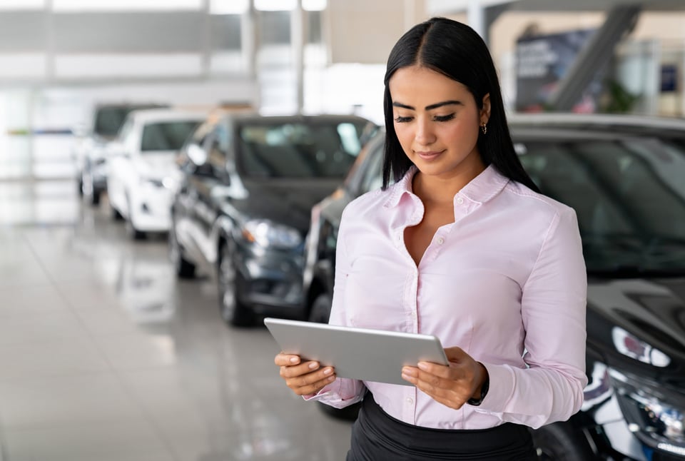 Car saleperson working in the showroom on a tablet.