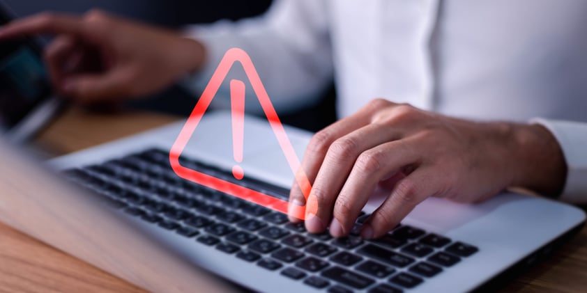 Man using computer laptop with triangle caution sign. 